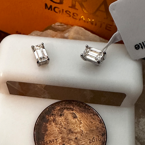 Diamond earrings on a white stand with a U.S. penny below