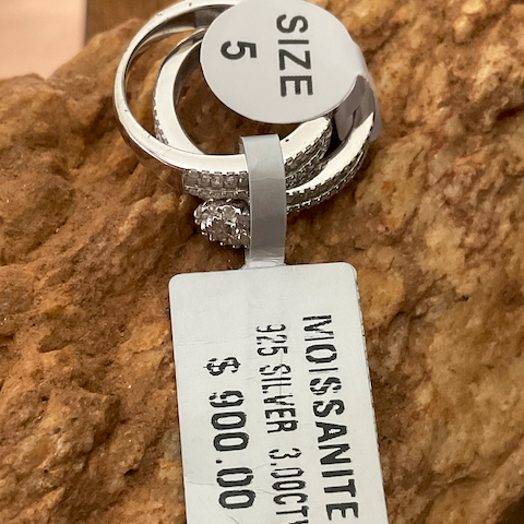Silver ring with a Moissanite stone on a rock, accompanied by a price tag.