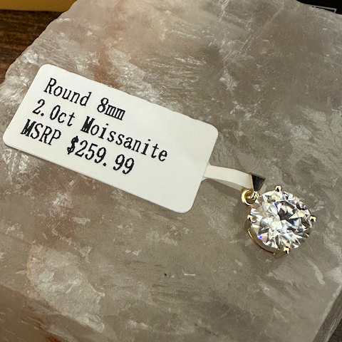Diamond pendant on a rock with a label detailing the stone's specifications.