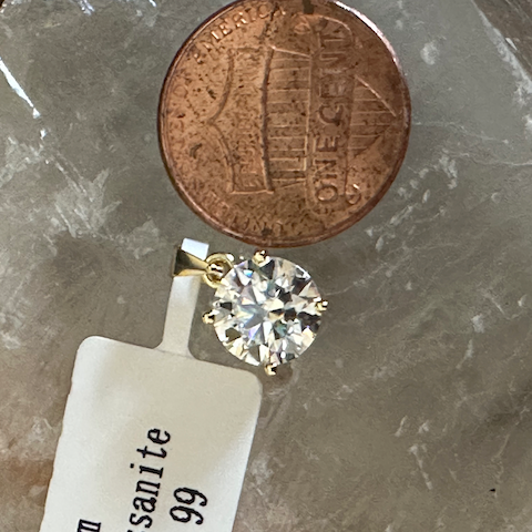 Diamond earring next to a penny on a crystal surface with a 'sanite' tag.