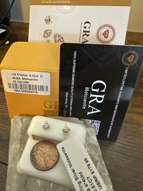 Diamond earrings with a GRA Moissanite card and box on a wooden surface