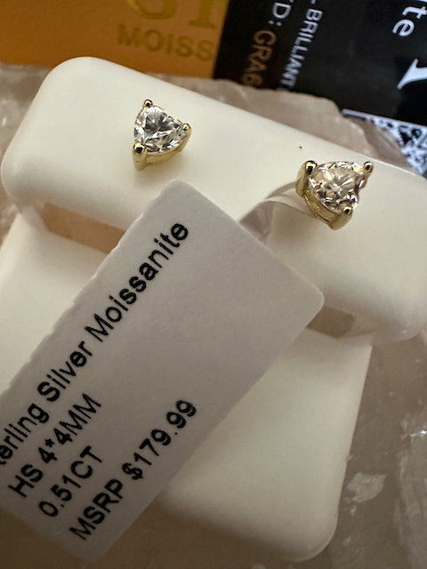 Pair of diamond stud earrings on a white stand with a label indicating 'Silver Moissanite' and price.