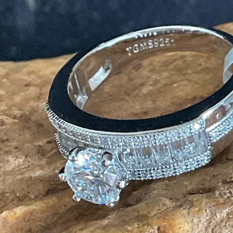 Silver ring with a large diamond and smaller diamonds on a stone surface