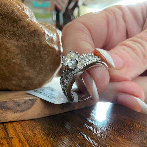 Close-up of a hand wearing two diamond rings on a wooden surface.