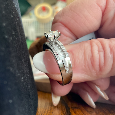Close-up of a hand holding two diamond rings on a wooden surface.