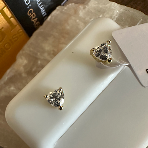 Heart-shaped diamond earrings on a white display card with a blurred background.