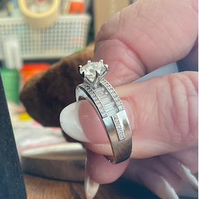 Hand holding a silver ring with a diamond on a wooden surface