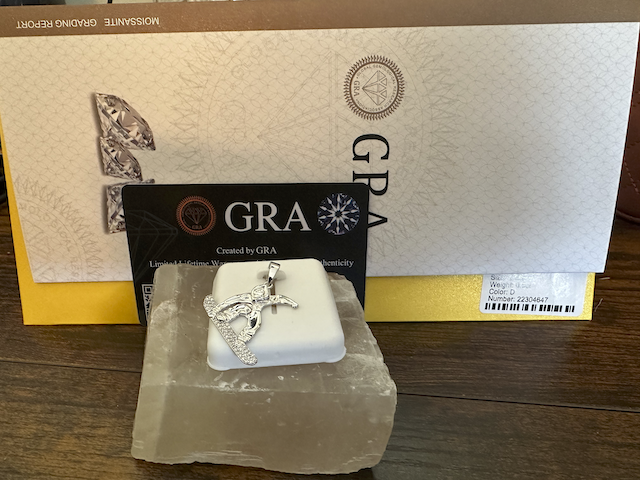 Silver cross pendant on a white stand with 'GRA' branding in the background