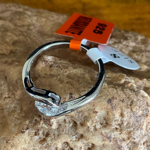 Silver ring with diamonds on a rock surface, featuring a price tag.