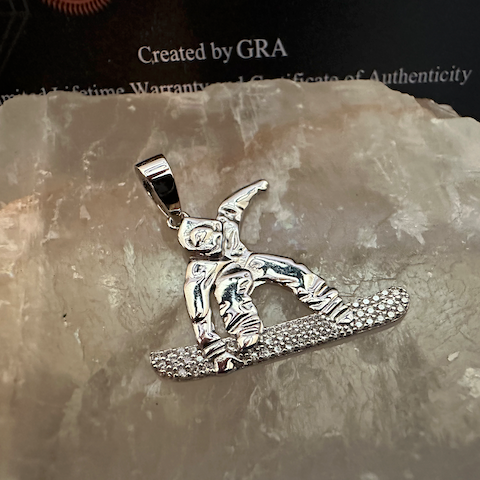 Silver snowboarding pendant on a stone surface with 'GRA' branding.