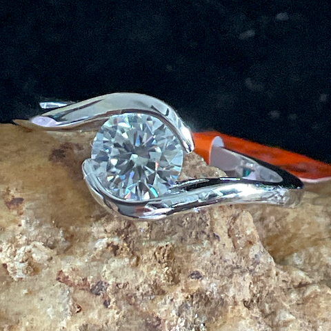 Diamond ring with orange and silver band on a textured surface