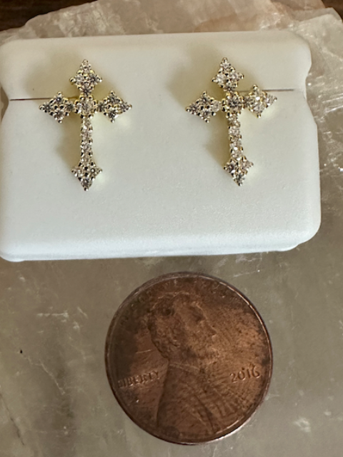 Silver cross-shaped earrings on a white stand with a penny for scale on a marble surface.