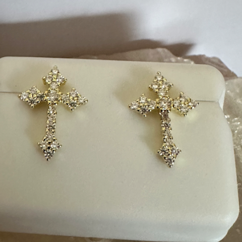 Pair of diamond-cross earrings on a white stand with a neutral background