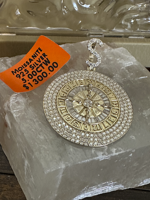 Decorative pendant with gemstones on a clear stand, price tag visible.