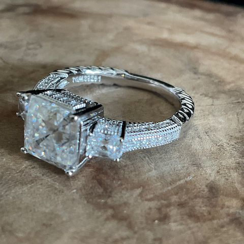 Silver ring with a large diamond and smaller stones on a textured surface