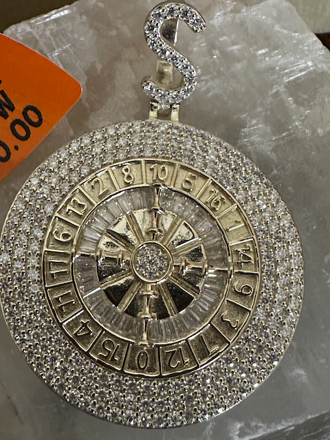 Gold roulette wheel pendant with gemstones on a gray background