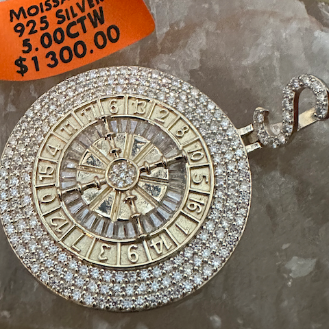 Silver pendant with gemstones on a gray surface, accompanied by an orange price tag.