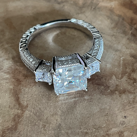 Silver ring with square-cut gemstones on a brown surface