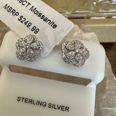 Pair of silver earrings on a white stand with 'Sterling Silver' label, against a blurred background.