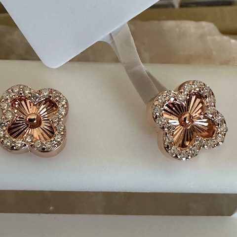 Rose gold flower-shaped earrings with gemstones on a white stand labeled 'MOISSANITE'.