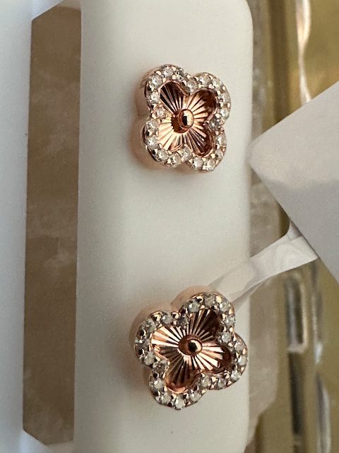 Rose gold floral earrings with clear gemstones on a white stand.