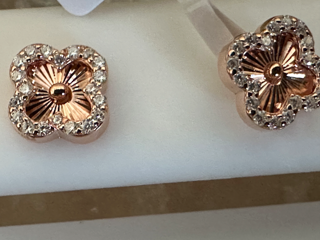 Rose gold flower-shaped earrings with clear stones on a white stand.