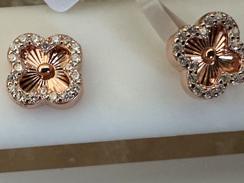 Rose gold flower-shaped earrings with clear stones on a white stand.