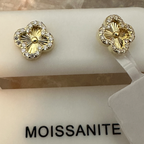 Gold flower-shaped earrings with clear stones on a white stand labeled 'Moissanite'.