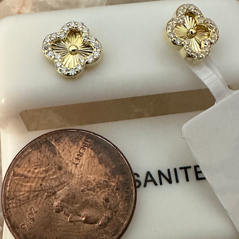 Gold floral earrings on a white surface with a penny for scale.