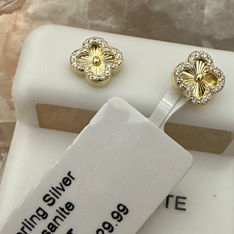 Gold earrings on a white stand with a price tag displaying details.