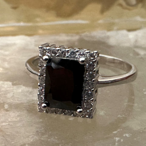 Silver ring with a black gemstone and diamond accents on a textured surface.
