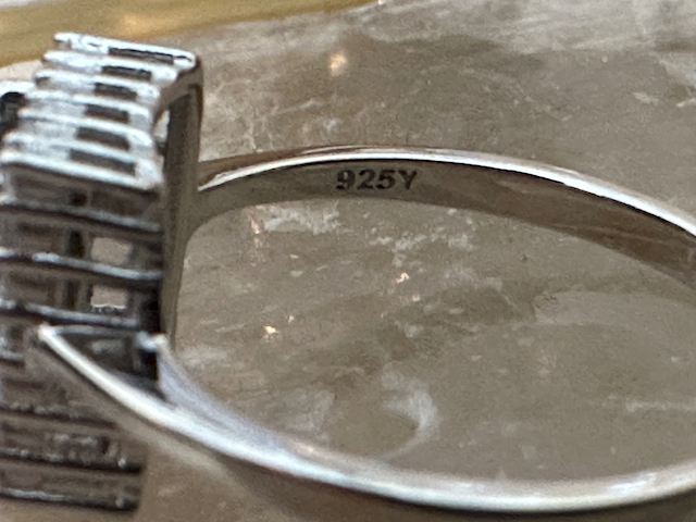 Close-up of a silver ring with '925' stamp on a reflective surface