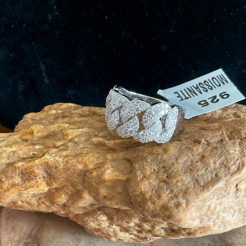 Silver ring with gemstones on a rock with a label in the background