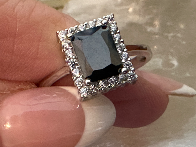 Silver ring with a dark gemstone held between fingers against a neutral background
