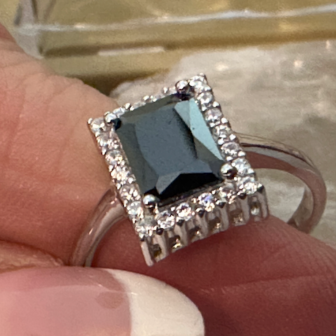 Ring with a black gemstone and diamond accents on a finger