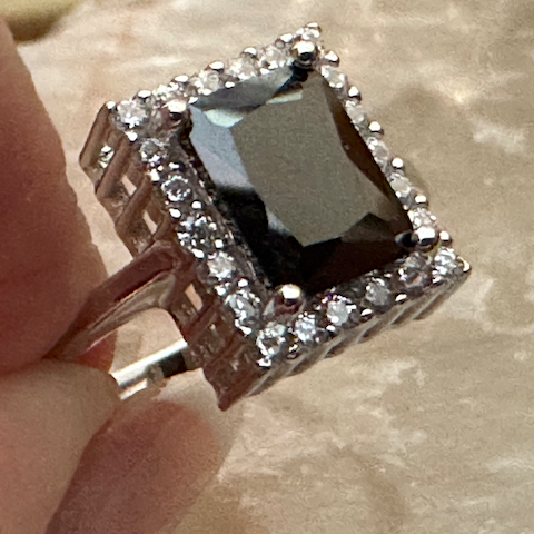 Silver ring with a dark stone held by a hand on a textured surface