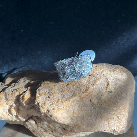 Silver ring with gemstones on a rock against a dark background