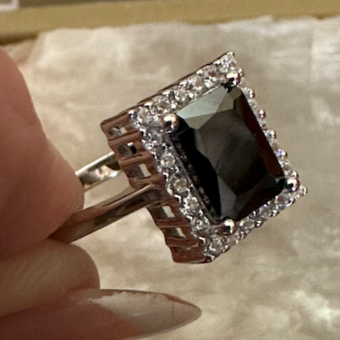 Ring with a large black gemstone and smaller clear stones held by a hand on a light background