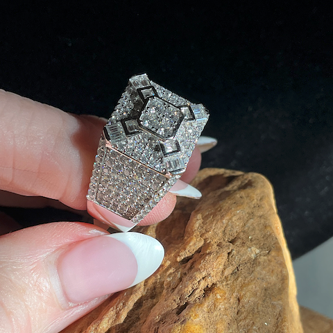 Diamond ring held by a hand against a dark background