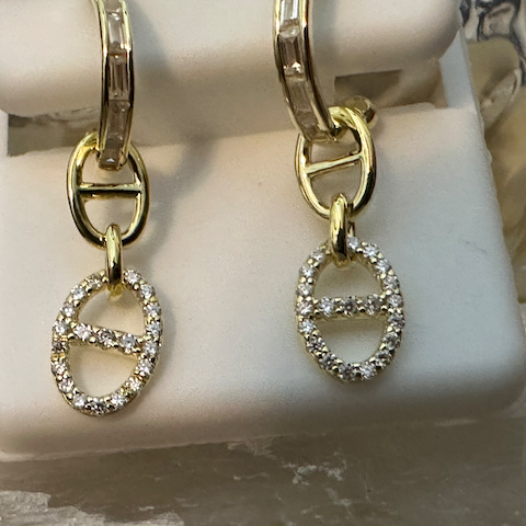 Gold hoop earrings with diamond-studded 'H' charms on a white stand.
