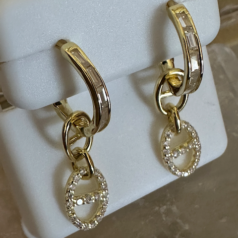 Gold hoop earrings with dangling charms on a white stand.