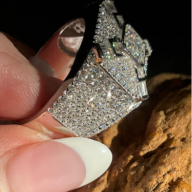 Silver ring with gemstones held by a hand against a textured brown background