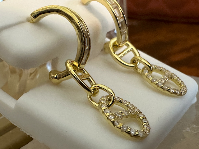 Gold hoop earrings with diamond-like stones on a white stand.