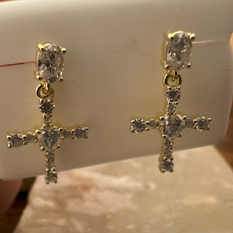 Gold cross earrings with clear stones on a white card held by a hand.
