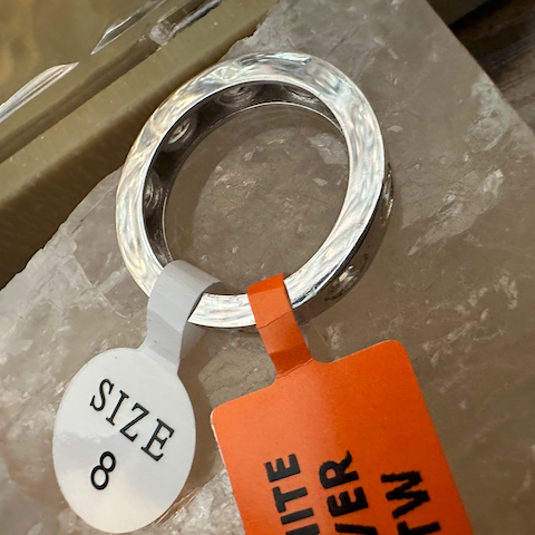 Silver ring with a size 8 tag and orange band on a marble surface