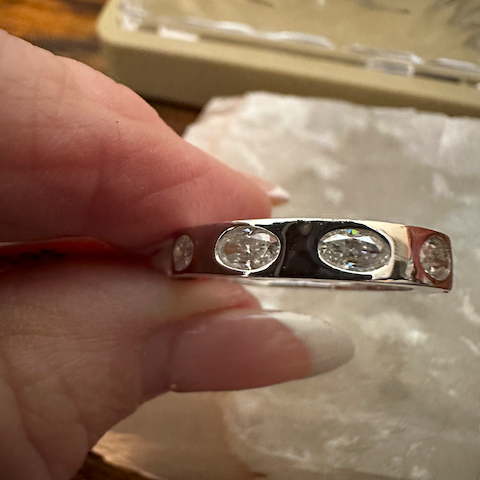 Silver ring with three diamonds held by a hand on a textured surface