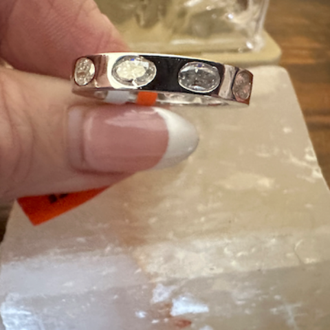Silver ring with small stones held by a hand on a wooden surface