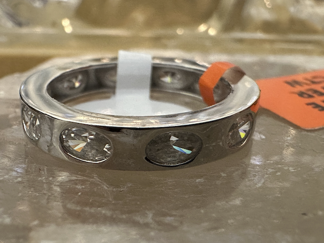 Silver ring with embedded stones on a reflective surface