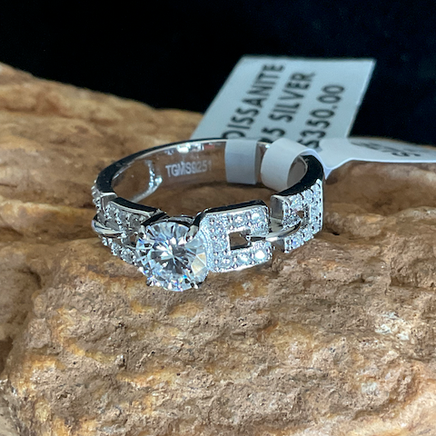 Silver ring with gemstone on a rock with a visible price tag.