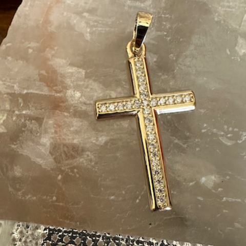 Gold cross pendant with Moissanite stones on a stone surface, accompanied by an orange tag with product details.